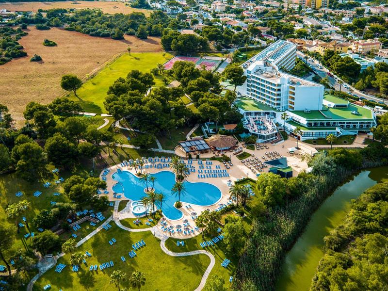 Große Hotelanlage mit mehreren Pools, Liegestühlen, umgeben von grünen Bäumen und Flussufer.