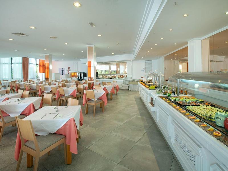 Großer, heller Speisesaal mit gedeckten Tischen und langer Buffettheke mit vielfältigen Speisen.