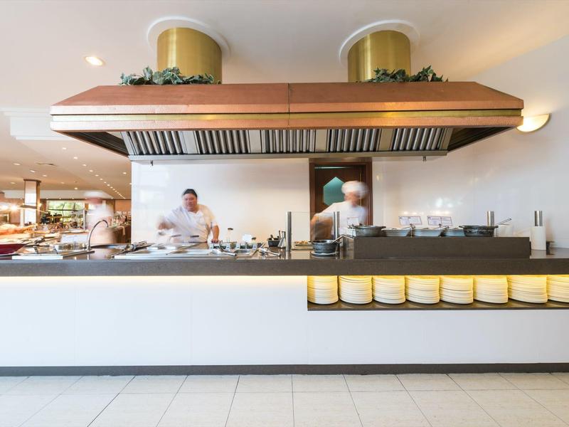 Kleine moderne Küche mit Kochinsel, zwei Köchen, Holz-Dunstabzug und weißen Wänden und Böden.