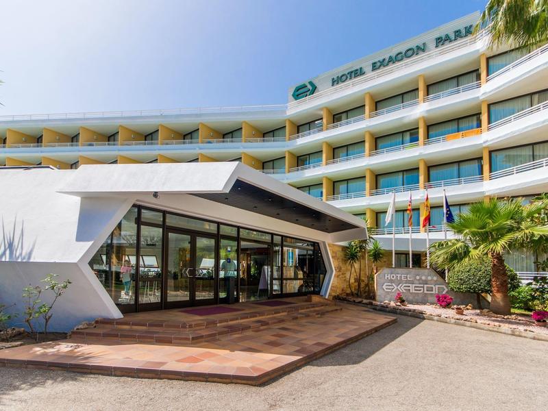 Modernes, mehrstöckiges Hotelgebäude mit Glasfront und begrüntem Eingangsbereich bei sonnigem Wetter.