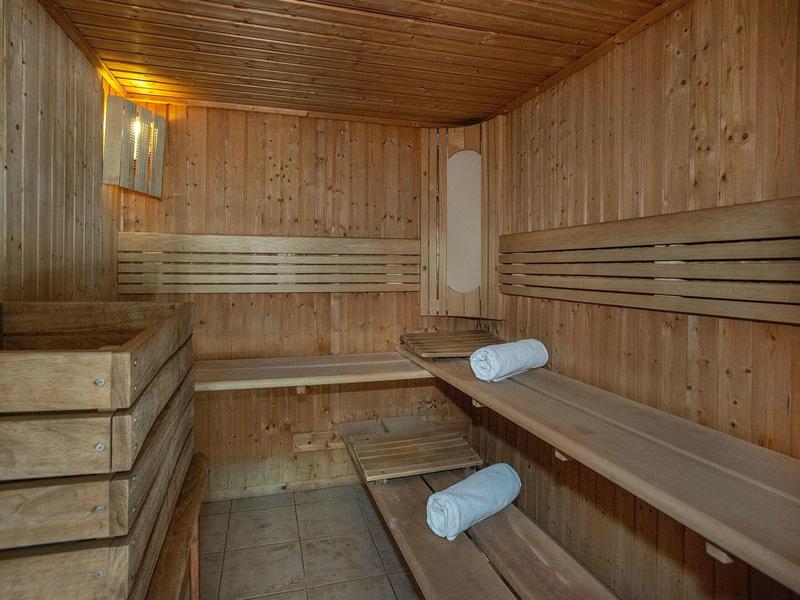 Holzsauna mit Bänken, zwei Handtüchern und warmer Beleuchtung an der Decke und Wand.