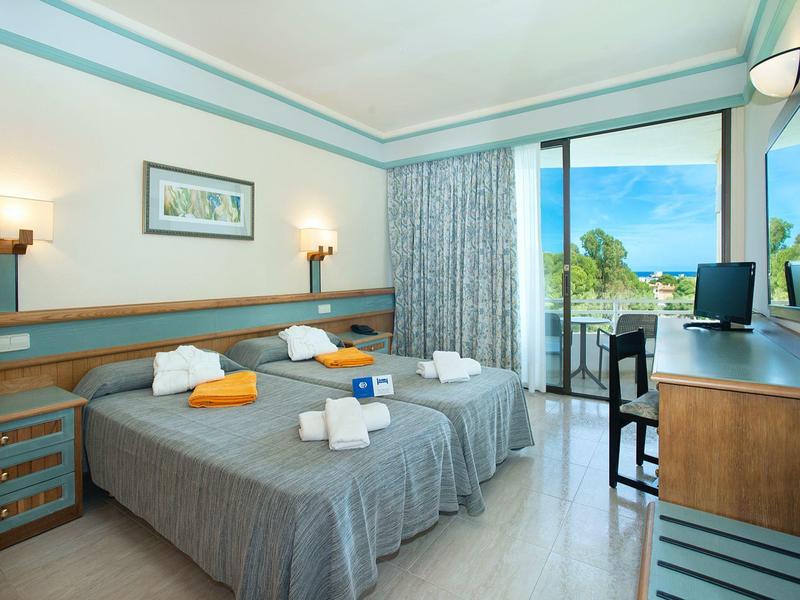 Hell eingerichtetes Hotelzimmer mit zwei Einzelbetten, Schreibtisch, Balkon und Meerblick.