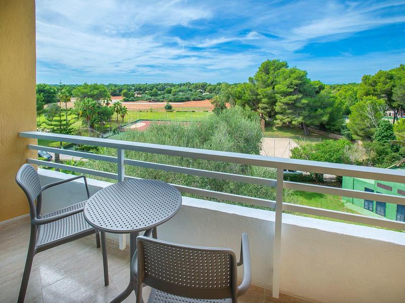 Balkon mit zwei grauen Stühlen und kleinem runden Tisch, Blick auf grüne Bäume und blauen Himmel.