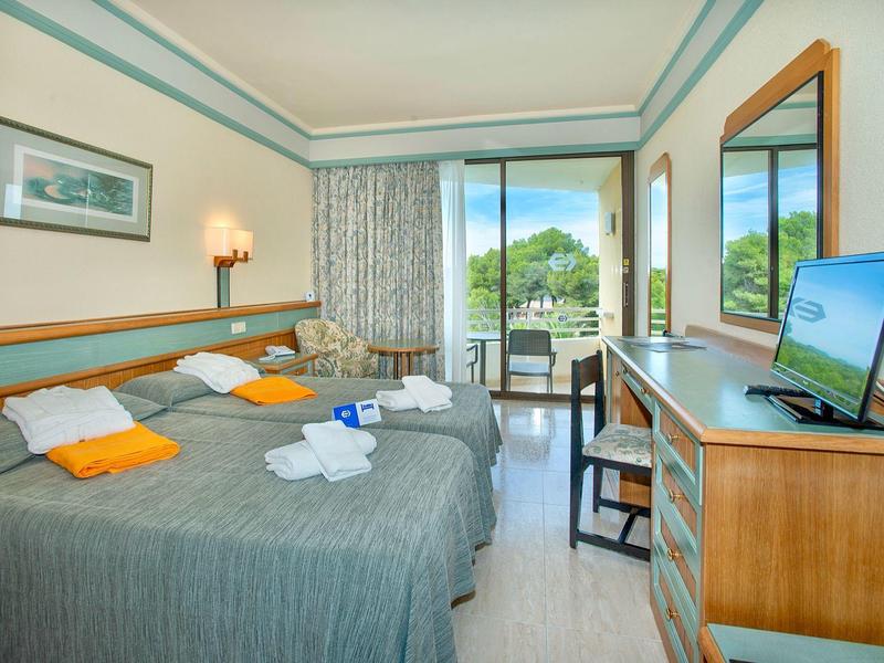 Hell eingerichtetes Hotelzimmer mit zwei Betten, TV, Balkon und Blick ins Grüne.