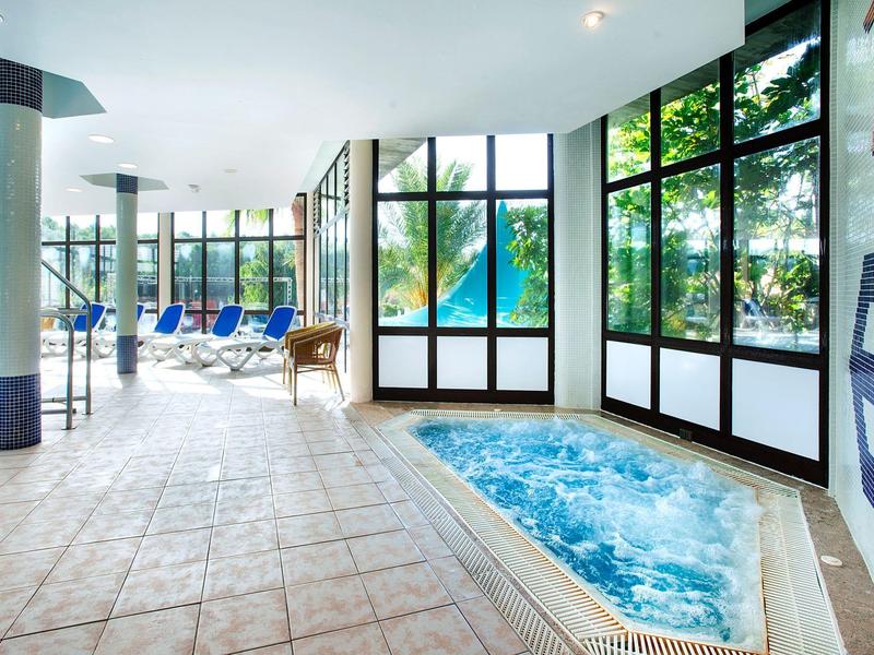 Helles Schwimmbad mit großen Fenstern, mehreren blauen Liegestühlen und gefliestem Boden.