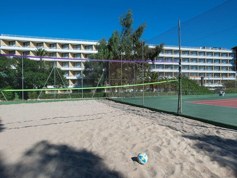Sandvolleyballfeld neben Tennisplatz mit mehrstöckigem weißen Gebäude im Hintergrund.