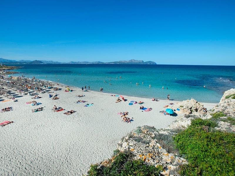 Weißer Sandstrand mit Sonnenschirmen, Liegestühlen, blauem Meer und klarem Himmel.