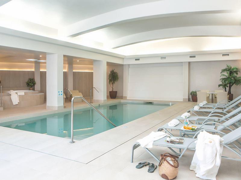 Interior with a rectangular indoor pool and lounge chairs in a modern wellness area.
