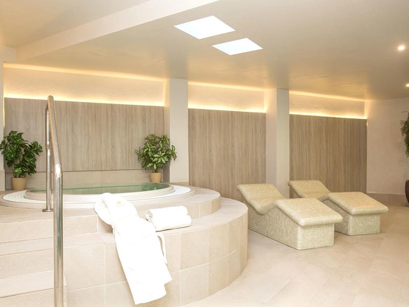 Bright spa area with a whirlpool, lounge chairs, and plants in a luxury hotel.