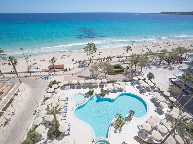 View of a pool with palm trees and a beach with turquoise water under clear skies.