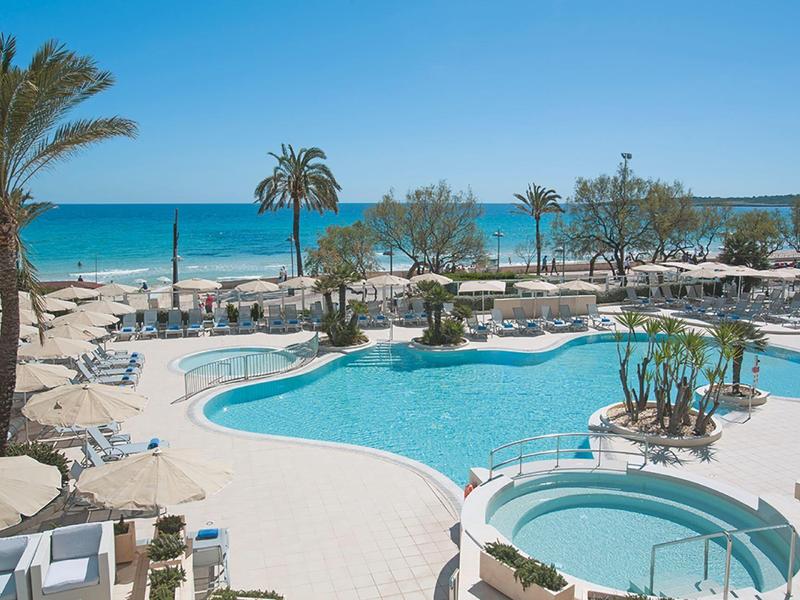 Hotel pool with sun loungers, palm trees, and view of the blue sea under clear sky