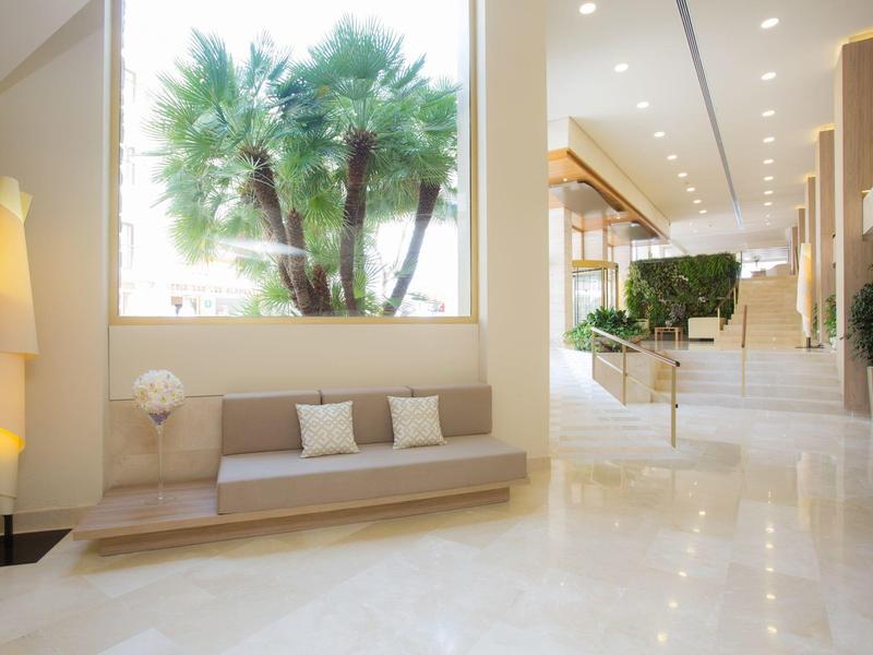 Modern hotel lobby with large window, bench seating, and green plants.