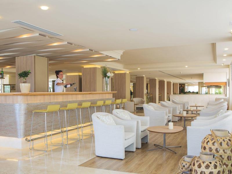 Modern hotel lounge area with white furniture and bar with yellow stools.