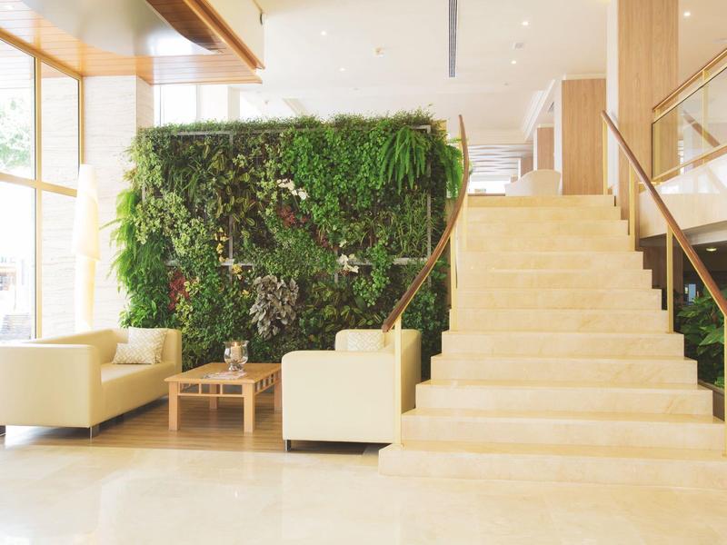 Bright hotel lobby with staircase, green wall, and comfortable armchairs beside a wooden table.