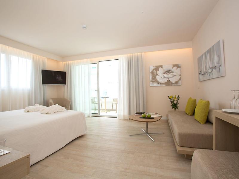 Bright hotel room with double bed, sofa, TV, and balcony with daylight.