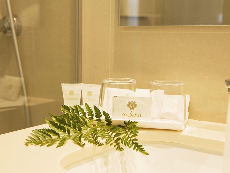 Bathroom shelf with toiletries, glasses, and a fern leaf on a white sink.