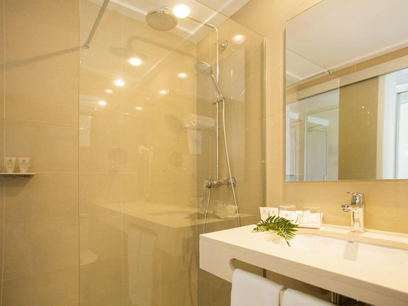 Bright bathroom with shower, sink, and large mirror in warm tones.