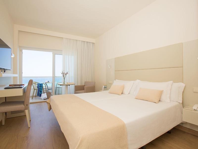 Bright hotel room with double bed, desk, balcony and sea view.