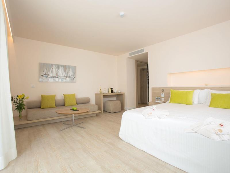 Bright hotel room with large bed, sofa, table, and minimalist decor.