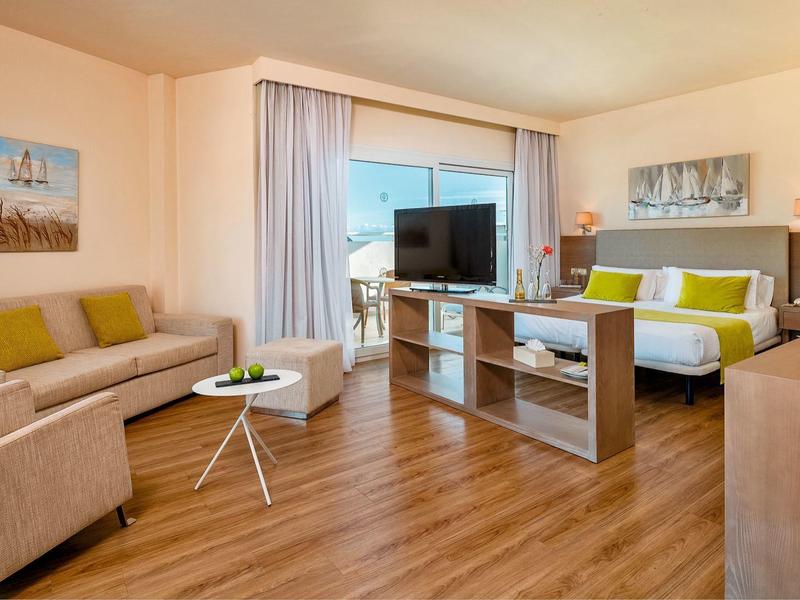 Modern hotel room with sofa, bed, TV, and large window with outdoor view.