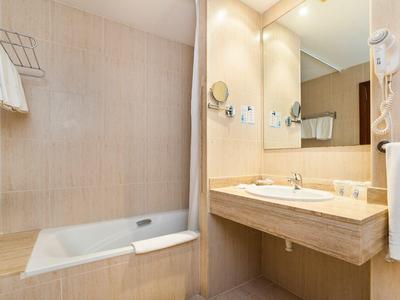 Světlá koupelna s vanou, moderním umyvadlem, zrcadlem a vysoušečem vlasů.