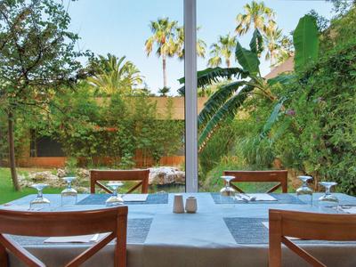 Tafel met witte doeken in een open tuinrestaurant met tropische planten.