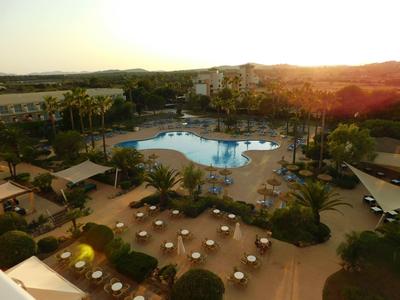 Hotelová oblast s bazénem obklopeným lehátky a stoly za západu slunce.