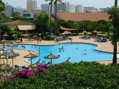 Hotelový bazén se slunečníky, lehátky a zelení v městském prostředí.