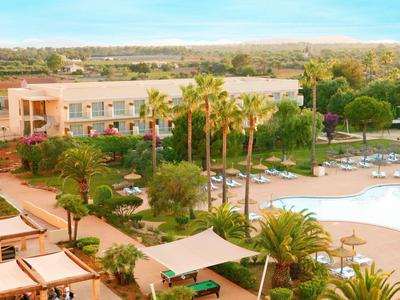 Hotel s bazénem, palmami a zahradou pod modrou oblohou.