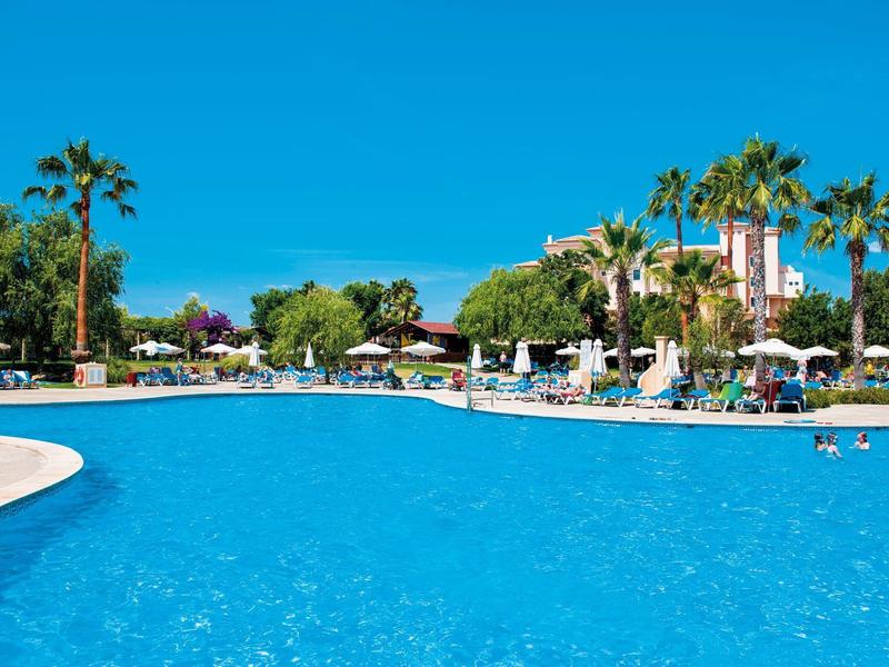 Velký bazén s lehátky a palmami pod jasně modrou oblohou.