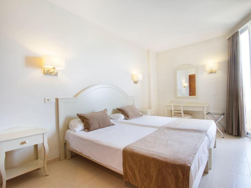 Světý hotelový pokoj se dvěma jednolůžky, nočními stolky a velkým oknem.