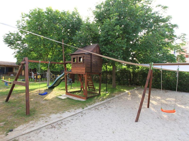 Dětské hřiště s lezeckou věží, skluzavkou, houpačkami a pískovištěm v hotelové zahradě.