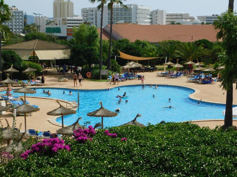 Hotelový bazén se slunečníky, lehátky a zelení v městském prostředí.