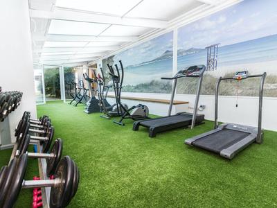 Heller Fitnessraum mit Trainingsgeräten und grüner Teppichausrüstung an der Wand
