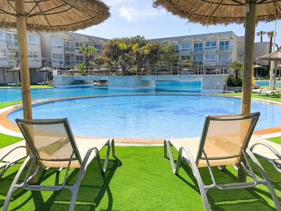 View of a hotel pool with lounge chairs and parasols on green grass.