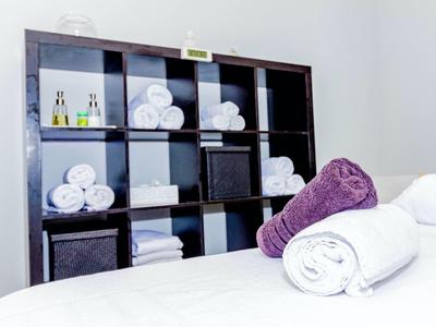 Stacked white and purple towels on table in front of black shelf with more towels and bottles.