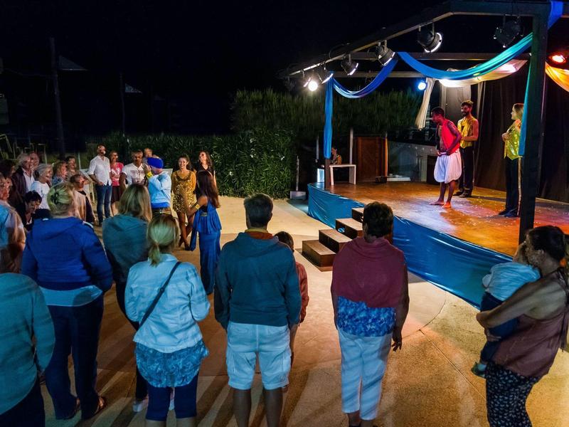 People watching a theater performance on an outdoor terrace at night.