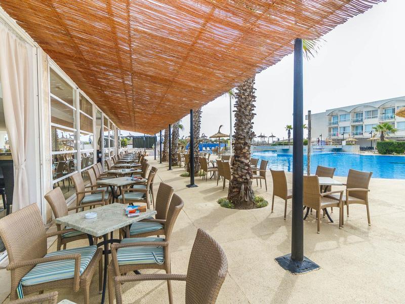 Outdoor seating area of a hotel next to a large pool and palm trees.
