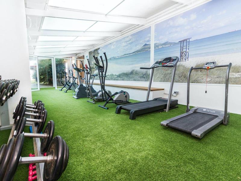 Gym with treadmills, elliptical trainers, and dumbbells on green carpet flooring.