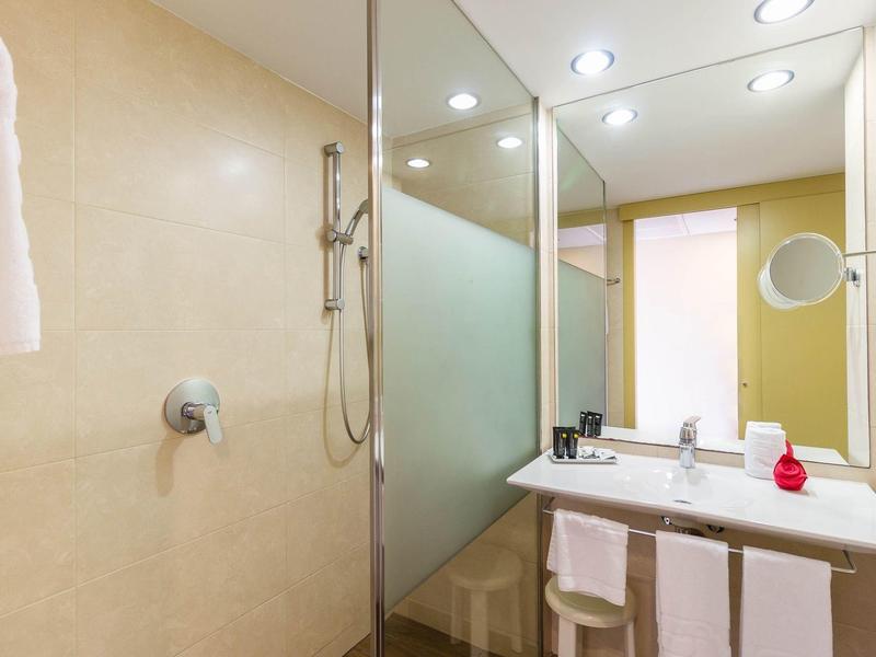 Modern hotel bathroom with shower, large mirror, and sink with towels.