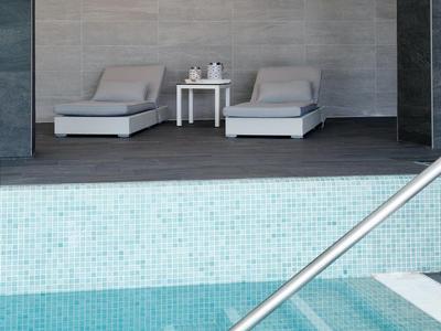 Nowoczesny basen z schodkami i dwoma szarymi leżakami obok małego stolika w pomieszczeniu.