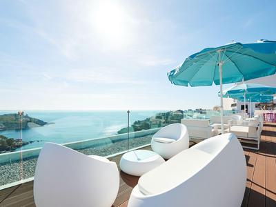 Moderne Terrasse mit weißen Möbeln und Meerblick bei sonnigem Wetter.