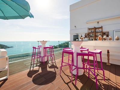 Modern outdoor hotel bar area with pink stools and sea view under sunshine.