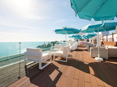 Hotel terrace with white furniture and turquoise umbrellas overlooking the sea.