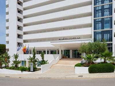 Modern white hotel building with elevator tower, palm trees, and ramps at the entrance.