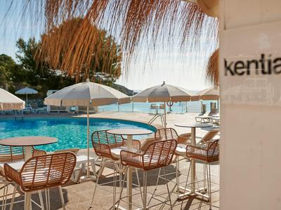 Seating area with chairs and tables beside a pool under umbrellas at a hotel.