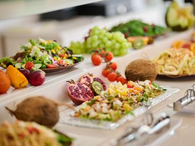 Buffet with various salads, fruits, and vegetables arranged on white plates.