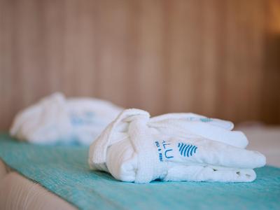 Crisp white bathrobe lies folded on a turquoise bedspread in a hotel room.