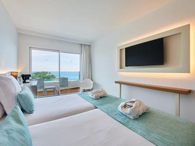 Modern hotel room with two beds, sea view, and minimalist design.