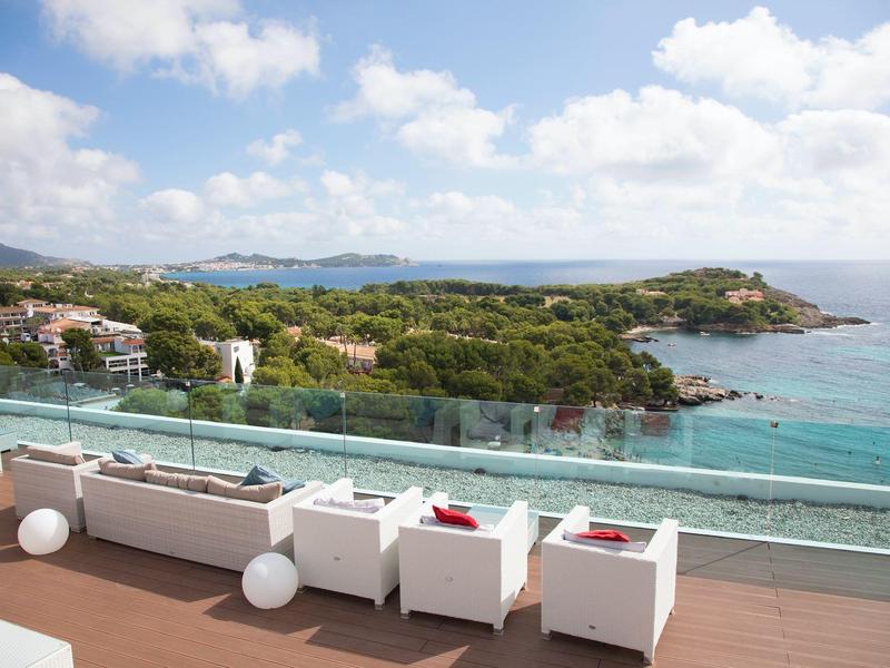 Balcon avec chaises blanches donnant sur une forêt côtière et la mer sous un ciel nuageux.